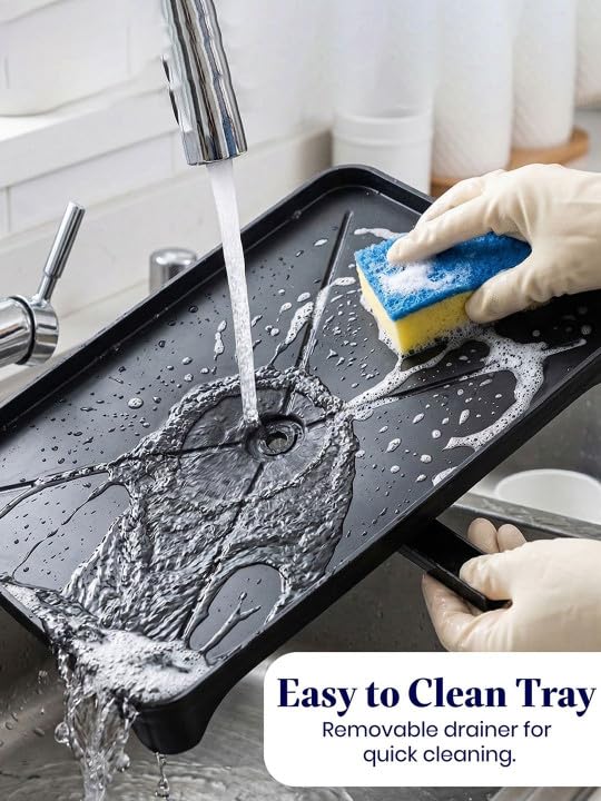 Removable black dish rack drain tray being rinsed and cleaned with a sponge in a kitchen sink